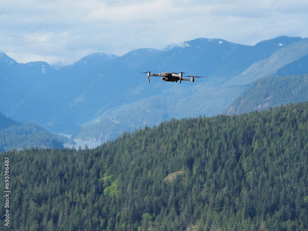 A drone flies with mountain, trees and water in the background. A drone flies with mountain, trees and water in the background.