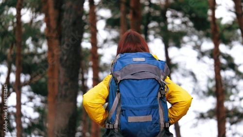 Curious woman carries rucksack containing travel essentials during forest walk. Young female takes leisurely stride through heart of forest. Concentrated lady hikes enjoying coniferous trees