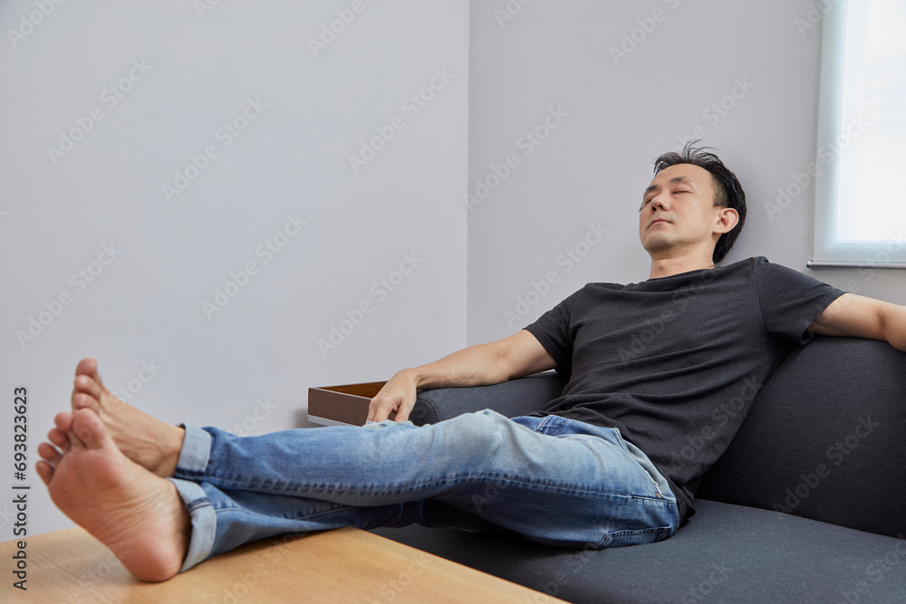 Old Asian man take a nap on grey sofa in a room. Old Asian man take a nap on grey sofa in a room.