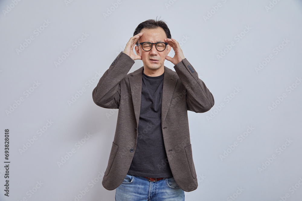 Portrait of stressed Japanese businessman in suit having headache on grey background. Portrait of stressed Japanese businessman in suit having headache on grey background.
