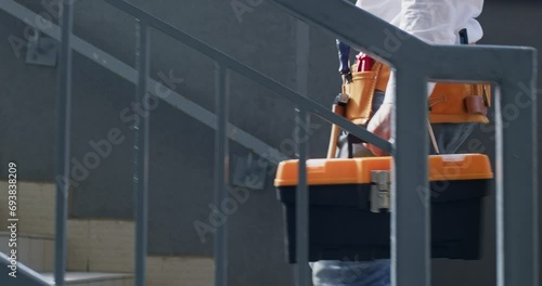 Worker walking across site with necessary equipment. Climbing upward worker with helmet and toolbox ensures well-prepared for work shift photo