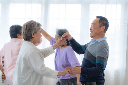 Asian Older male and females people dance with their partners on a dancing floor in living space. Happy older couple performing get exercise. Joyful carefree retired senior friends enjoying relaxation