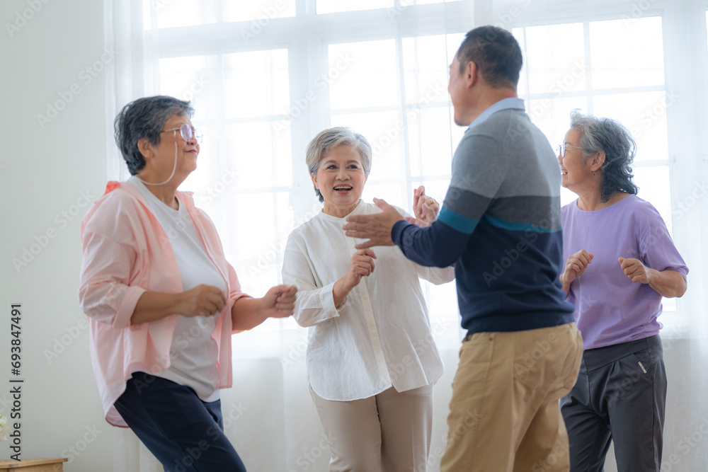 Fototapeta premium Asian Older male and females people dance with their partners on a dancing floor in living space. Happy older couple performing get exercise. Joyful carefree retired senior friends enjoying relaxation