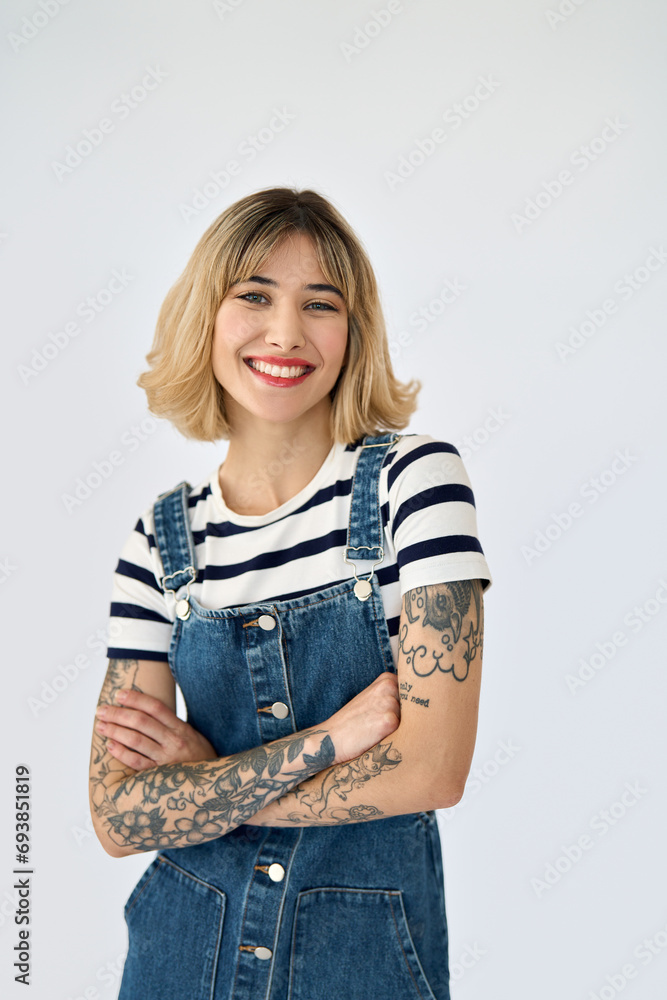Happy pretty gen z blonde young woman, cute smiling girl with short blond hair tattoos wearing striped t-shirt denim dress looking at camera standing isolated on white background. Vertical portrait. Happy pretty gen z blonde young woman, cute smiling girl with short blond hair tattoos wearing striped t-shirt denim dress looking at camera standing isolated on white background. Vertical portrait.