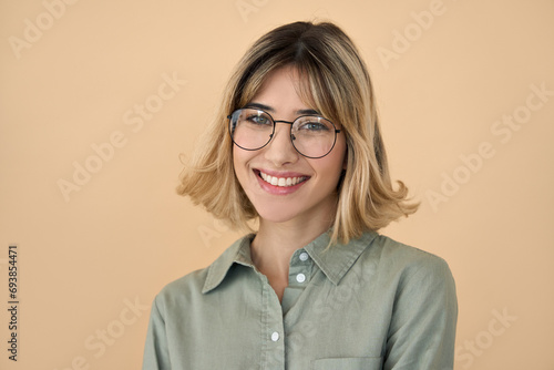 Smiling pretty gen z blonde young woman, happy college student girl with short blond hair wearing glasses looking at camera standing isolated on beige background. Close up headshot portrait.