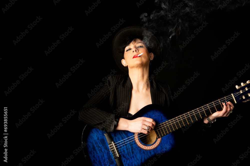 Young beautiful woman in black with a cigarette and an acoustic blue guitar Young beautiful woman in black with a cigarette and an acoustic blue guitar
