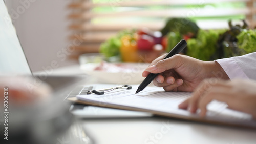 Professional nutritionist sitting at desk with fruit and vegetable working on diet plan photo