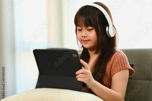 Happy little girl in headphones watching children content on digital tablet. Technology and childhood concept