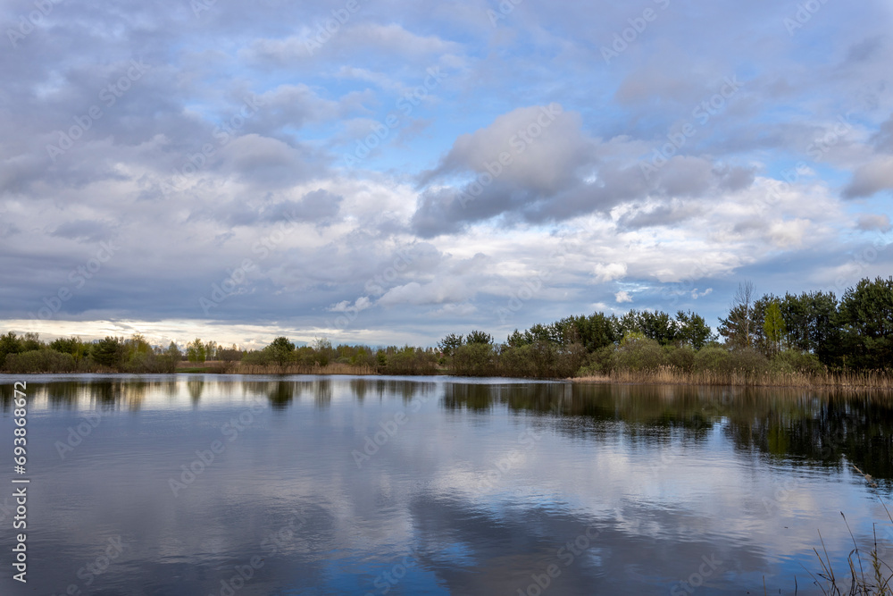 Spring landscape with clouds reflected in the water, young trees and shrubs on the horizon Spring landscape with clouds reflected in the water, young trees and shrubs on the horizon