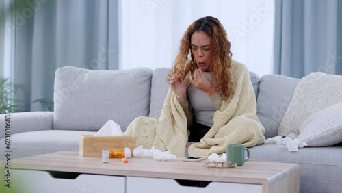 Sick woman suffering from covid, a flu virus or a cold infection during quarantine. Ill young female sneezing in lockdown on the couch at home, blowing her nose with a tisse photo