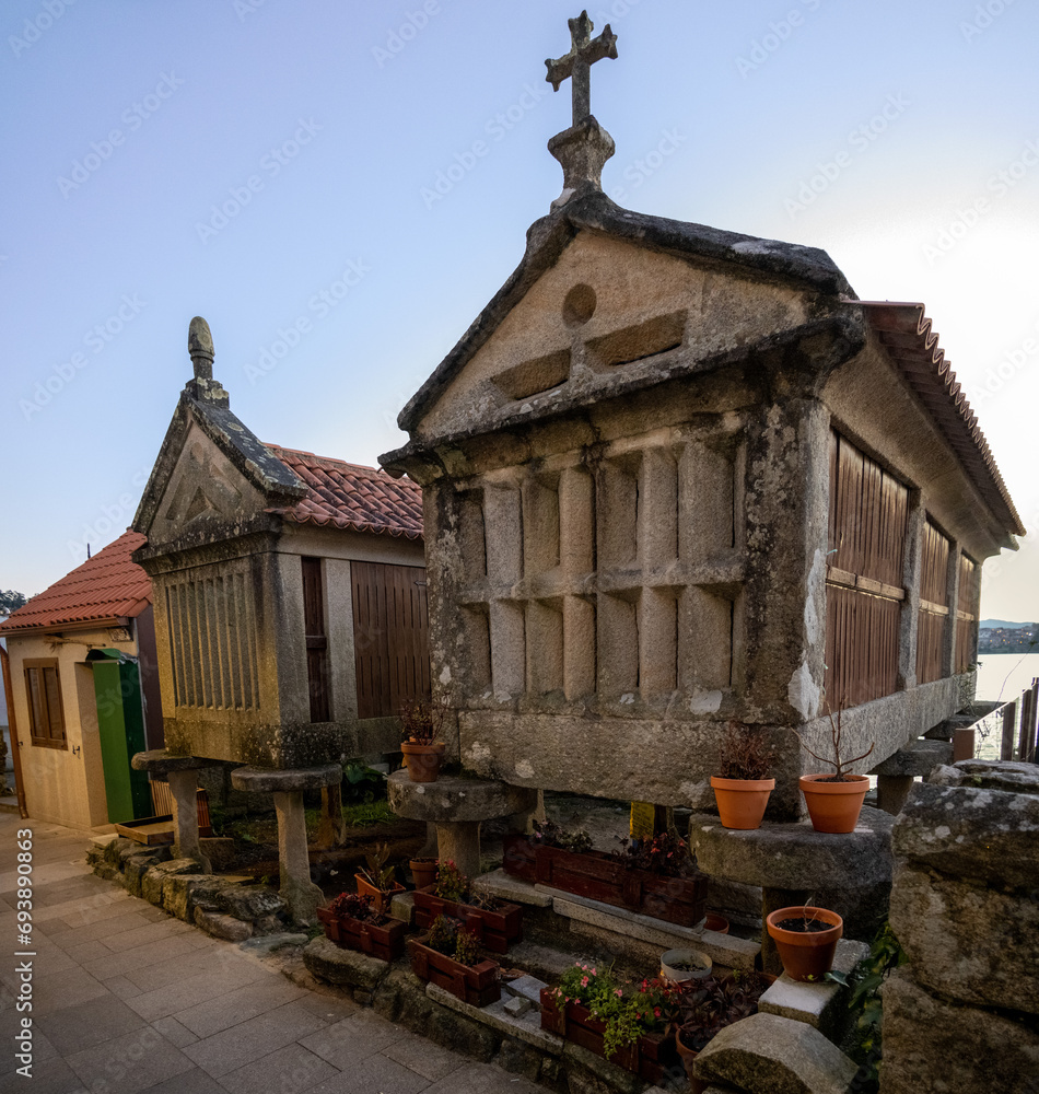 Traditional stone granaries (horreos) in Combarro, Galicia, Spain, with potted plants and a cross on the roof, near the sea.