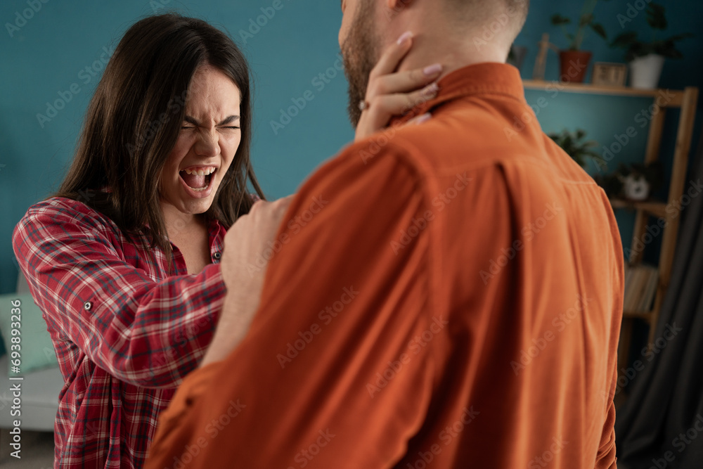 Female attacks man, domestic violence. Wife beats husband. An aggressive woman hits man and crying. Domination in couple - obrazy, fototapety, plakaty 