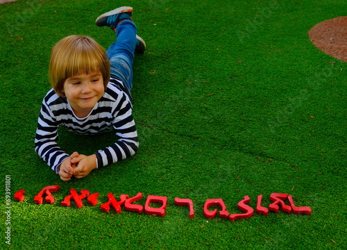 Letters of the Hebrew alphabet. A boy learns Hebrew. Ulpan for children, kindergarten, elementary school in Israel. Portrait of a child on a green background. photo