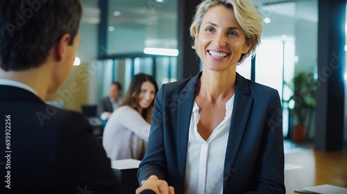 Handshake between smiling businesswoman and client at office meeting. Mid aged female manager or hr hiring new recruit, bank or insurance agent, or lawyer making contract deal at work
