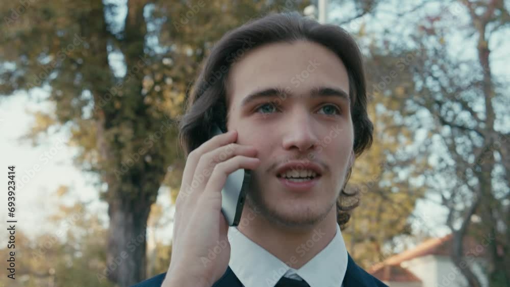 Man in a business suit is walking down the street and talking on the phone. A young man in a suit talking on a smartphone, slow motion. A smiling businessman in the city talking on a cell phone. Man in a business suit is walking down the street and talking on the phone. A young man in a suit talking on a smartphone, slow motion. A smiling businessman in the city talking on a cell phone.