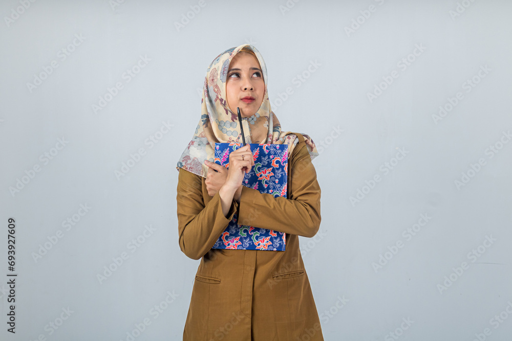 Young Indonesian Woman government employee wearing a brown uniform. was holding a large book and thinking looking at the direction of the negative space Young Indonesian Woman government employee wearing a brown uniform. was holding a large book and thinking looking at the direction of the negative space