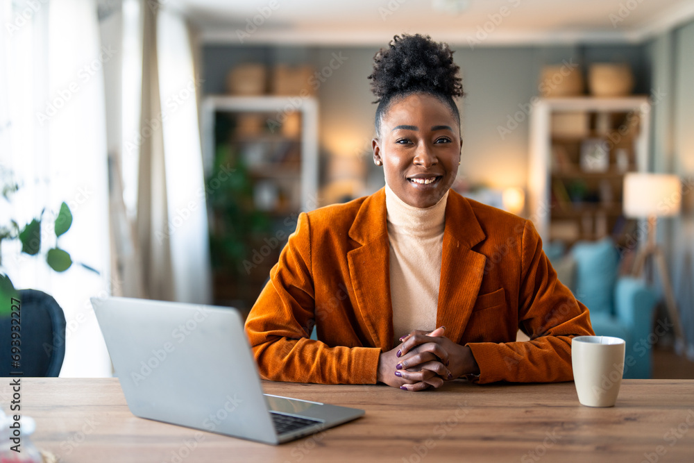 Smiling confident businesswoman looking at camera sitting at home office desk. Modern stylish female corporate employee successful executive manager with laptop posing for business portrait. Smiling confident businesswoman looking at camera sitting at home office desk. Modern stylish female corporate employee successful executive manager with laptop posing for business portrait.