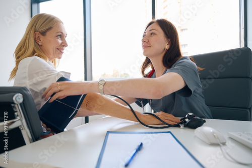 Family doctor preparing woman for blood pressure measurement