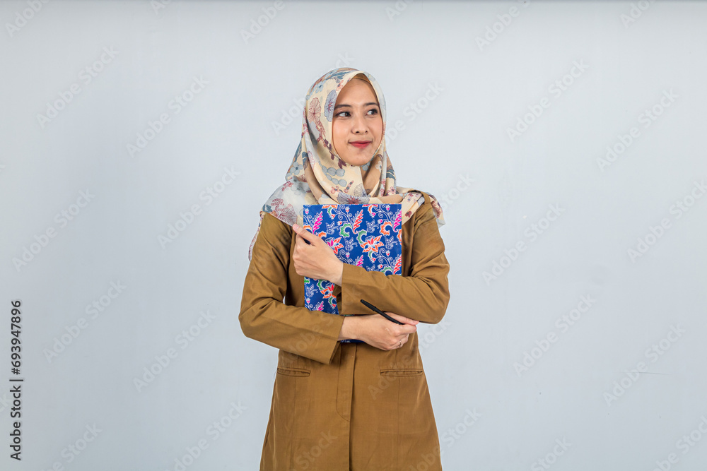 Young Indonesian Woman government employee wearing a brown uniform. was holding a large book and looking towards the negative space Young Indonesian Woman government employee wearing a brown uniform. was holding a large book and looking towards the negative space