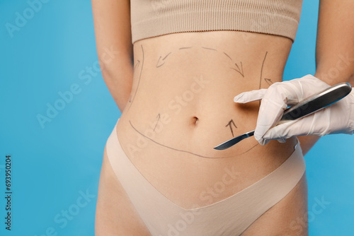 Doctor drawing dashed line marks on female body before plastic surgery operation. Isolated on blue background. Beauty care, anti aging procedures, plastic surgery concept