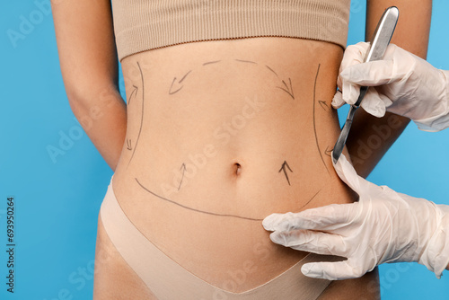 Close up of plastic surgeon using marker pen while marking body of female before plastic surgery. Isolated on blue background. Beauty care, anti aging procedures, plastic surgery concept