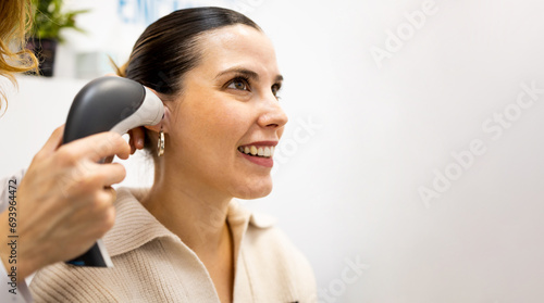 An unrecognizable female doctor uses otoscope to check the ear of a girl patient. Otoscopy and hearing check for people with hearing problems in audiology or hearing clinic. photo
