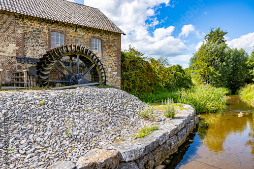 Geul river and old Eper or Wingbergermolen water mill, stone building with two windows, trees and wild vegetation in background, sunny day at Terpoorterweg, Epen, South Limburg, Netherlands photo