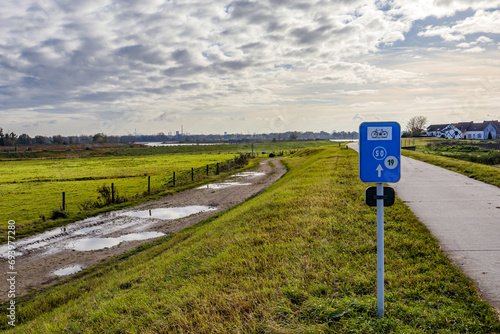 Bike path in Belgian nature reserve De Wissen, between a hiking trail with puddles and countryside, farms in background, routes 50 and 19, cloudy day with cloud-covered sky in Dilsen-Stokkem, Belgium photo