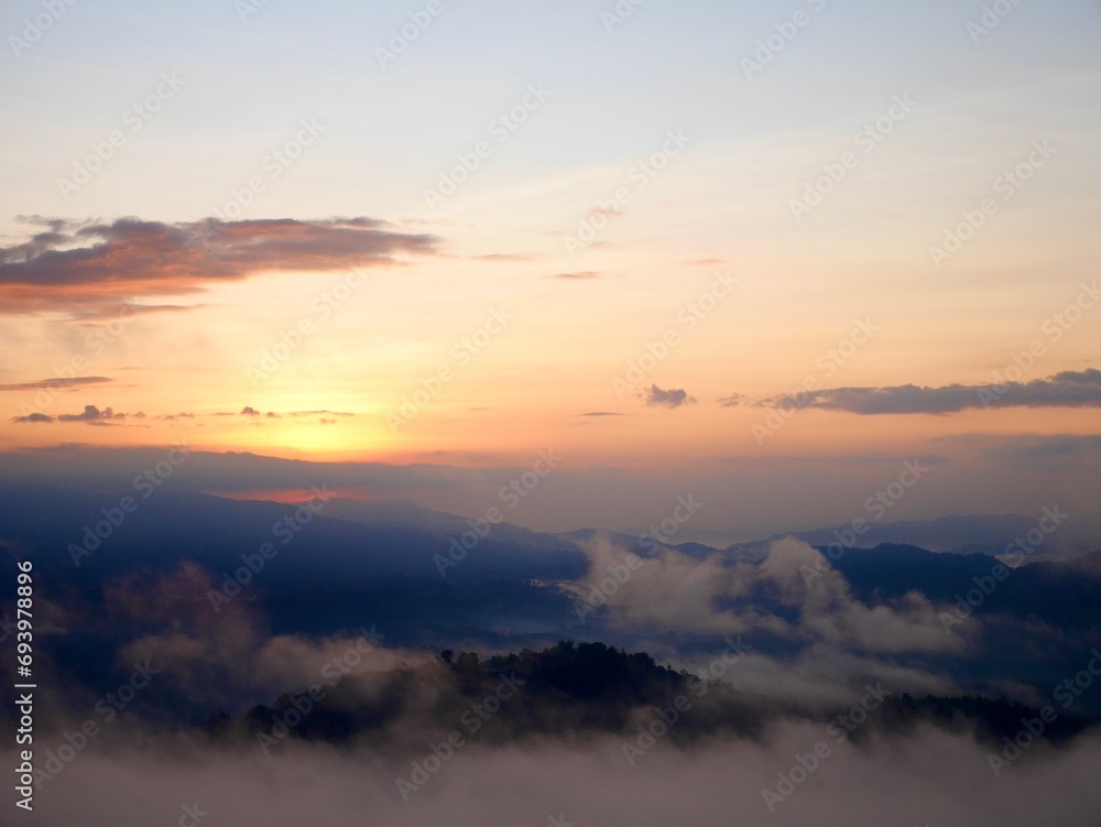 The mist flows through the mountain forest, Sun shining into tropical forest, Mist drifts through mountain ridges in the morning, slow floating fog blowing cover on the top of mountain