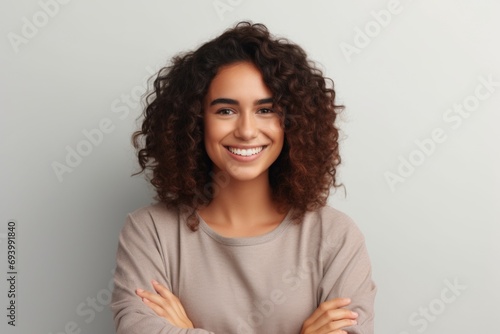 A woman with curly hair smiling  confidently standing with her arms crossed. Perfect for showcasing positivity and self-assurance. Ideal for websites  blogs  and promotional materials