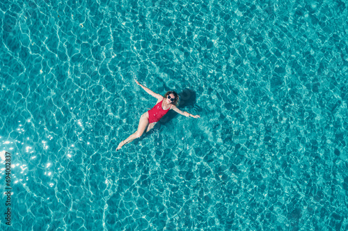 Top view of young pretty sexy girl in red swimsuit floating on water surface in crystal clear turquoise ocean. Happy island lifestyle. © Evgenii Bakhchev