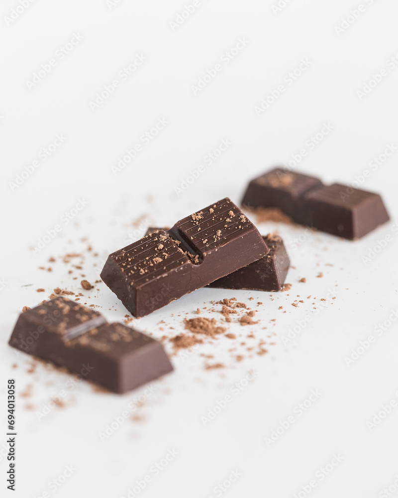 Pieces of chocolate on white background with cocoa powder Pieces of chocolate on white background with cocoa powder