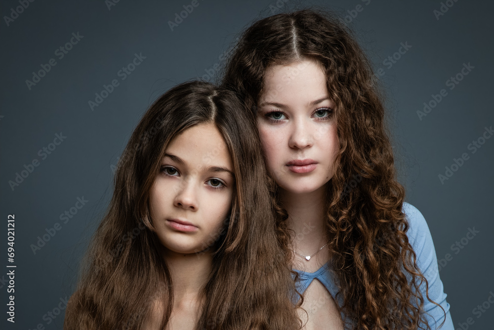Studio portrait of two beautiful sisters in blue shirts and jeans against gray background. Studio portrait of two beautiful sisters in blue shirts and jeans against gray background.