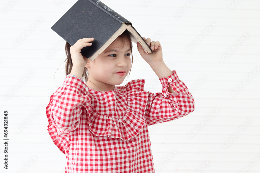 Happy smiling Asian girl holding and playing with a book, standing on white wall room. Cute child with a book, kid education and reading. Happy smiling Asian girl holding and playing with a book, standing on white wall room. Cute child with a book, kid education and reading.