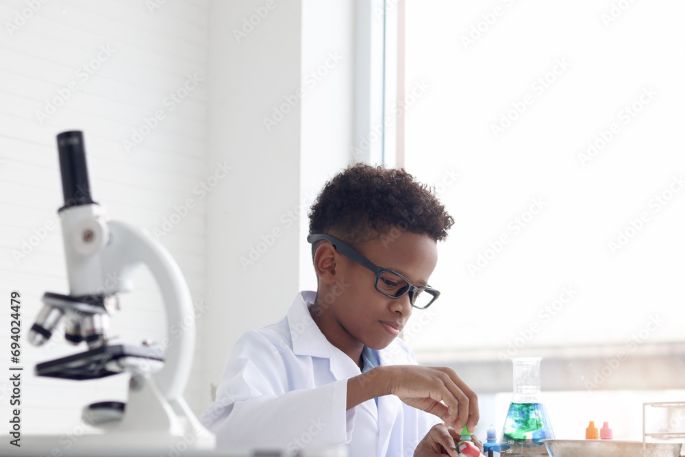 Happy smiling African boy in lab coat doing science experiments, young schoolboy kid scientist having fun in chemistry laboratory class, little child doing research at school. Happy smiling African boy in lab coat doing science experiments, young schoolboy kid scientist having fun in chemistry laboratory class, little child doing research at school.
