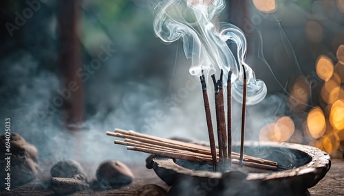 Incense sticks emit swirling smoke against a soft-focus, bokeh-lit background. The image evokes a sense of spirituality and relaxation with the smoke gently rising in the air photo