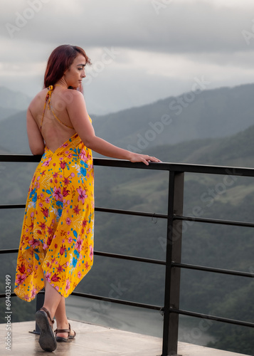 mujer con vestido amarillo en un mirador observando las montañas.