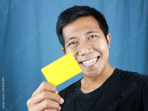 Happy funny face expression Asian man holding empty card on blue background. Transaction concept photo