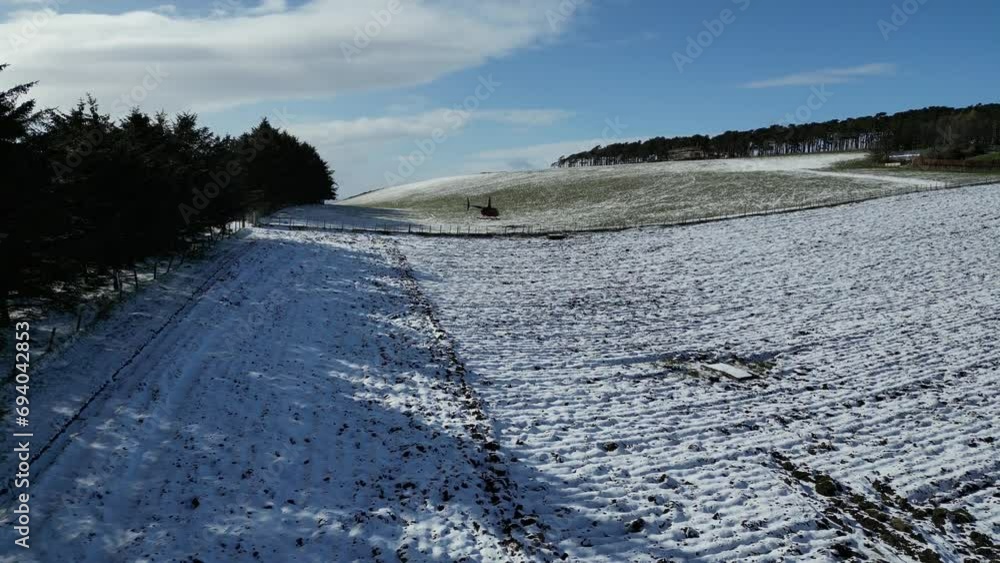 Distant shot of helicopter taking off in field meadow snow winter covered landscape departing take off Distant shot of helicopter taking off in field meadow snow winter covered landscape departing take off