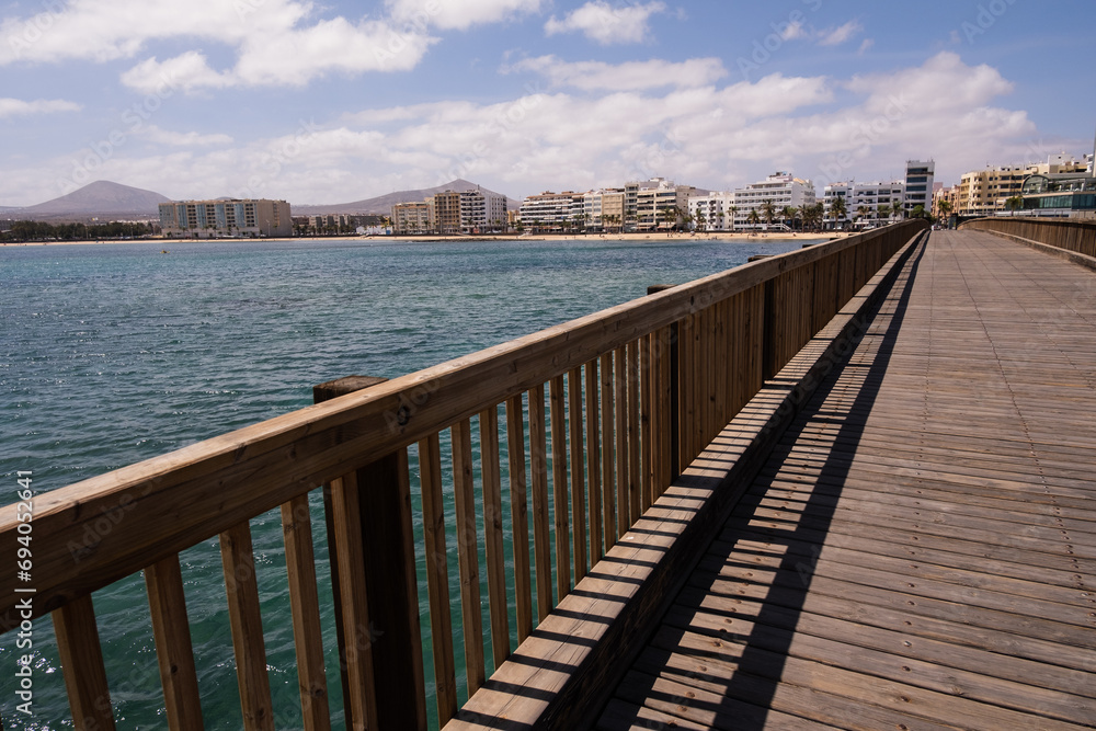 View of the city of Arrecife from the Fermina islet, from a wooden bridge. Turquoise blue water. Sky with big white clouds. Seascape. Lanzarote, Canary Islands, Spain.