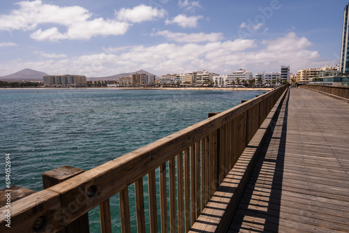 View of the city of Arrecife from the Fermina islet, from a wooden bridge. Turquoise blue water. Sky with big white clouds. Seascape. Lanzarote, Canary Islands, Spain. © Jess
