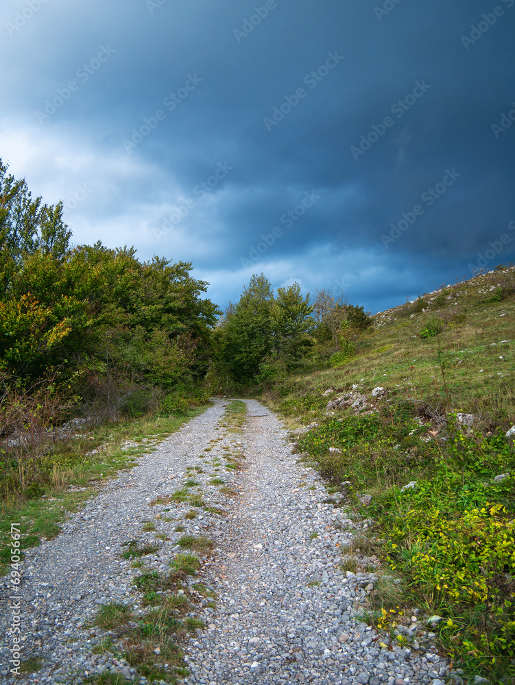 Unpaved road under storm clouds through the hilly woodland of the Croatian Mountains.
