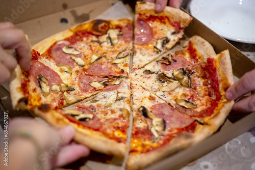 large pizza on the table in a box, cut into pieces, which people take with their hands at the feast.