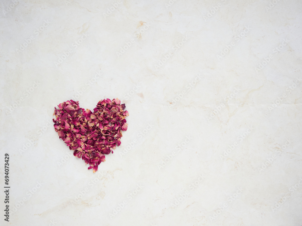 A lot of small dried red rose petals forming a heart on beige paper with copy space. Romantic concept for Valentine's Day postcards.