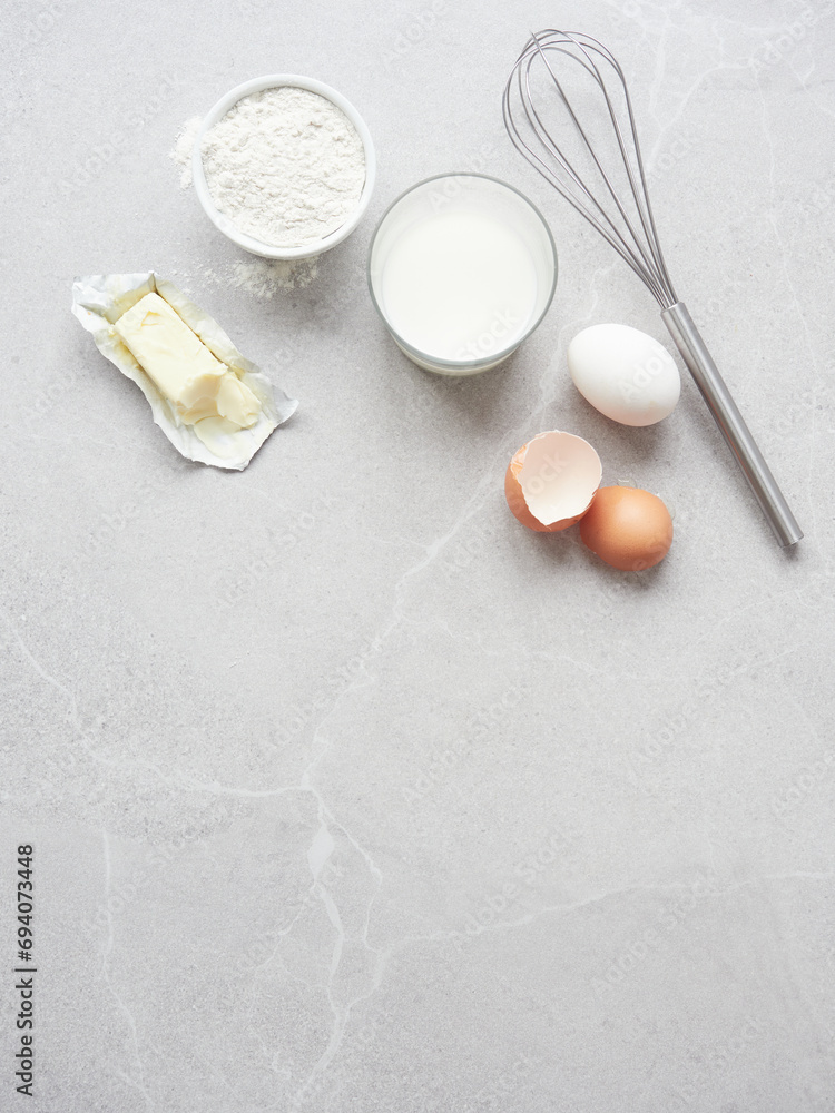 Ingredients for homemade pastry: flour, milk, eggs and butter on gray stone table, hand metal whisk. Top view with copy space. Ingredients for homemade pastry: flour, milk, eggs and butter on gray stone table, hand metal whisk. Top view with copy space.