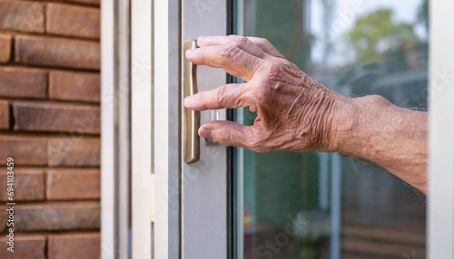 The hand of an elderly person clings to the glass door in front of the house. Feeling lonely and alone. life in retirement for the elderly