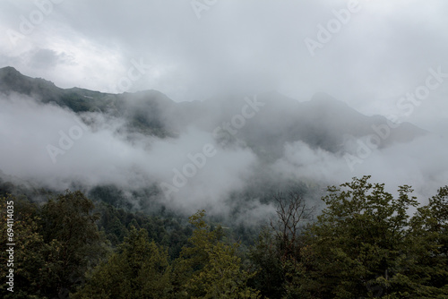 Fog and clouds in the mountains against the backdrop of the setting sun, changeable weather in the mountains, clouds and nebula on mountain peaks wide © daniiD