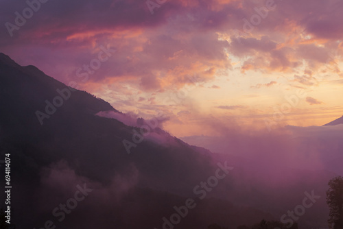Fog and clouds in the mountains against the backdrop of the setting sun, changeable weather in the mountains, clouds and nebula on mountain peaks wide © daniiD