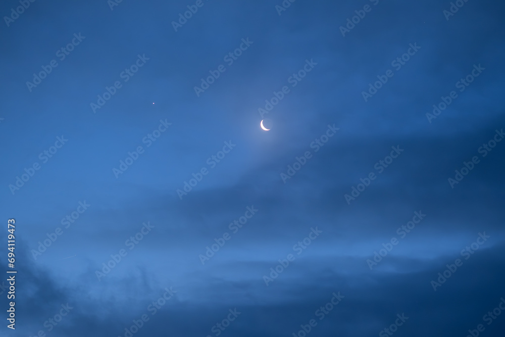 Night sky with old thin bright Moon and star Venus in the clouds, can be used as background.