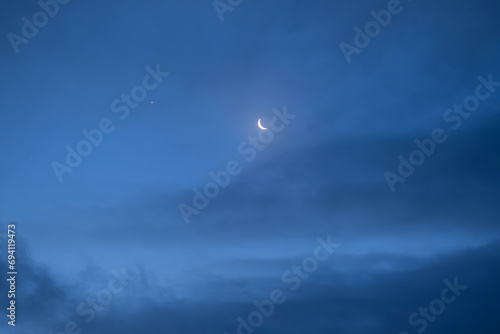 Night sky with old thin bright Moon and star Venus in the clouds  can be used as background.